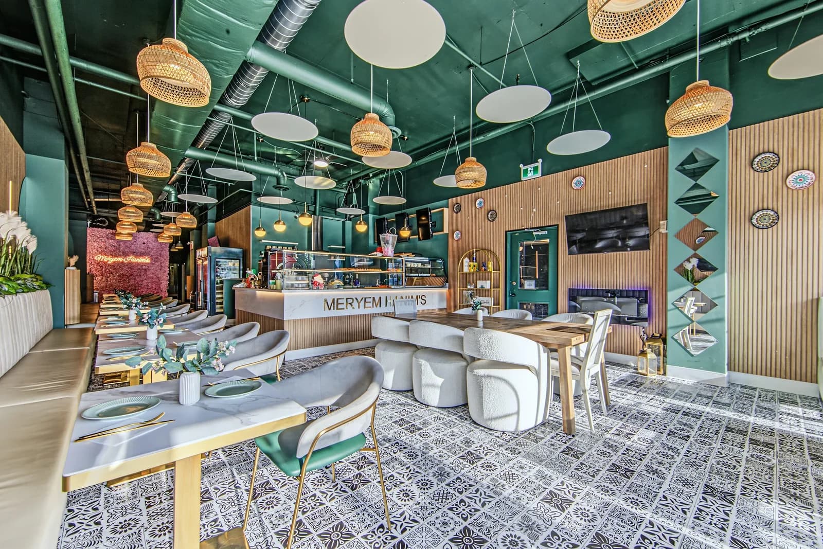 Café dining room with green walls, rattan pendant lights, wood slat panels, white chairs and a patterned tile floor