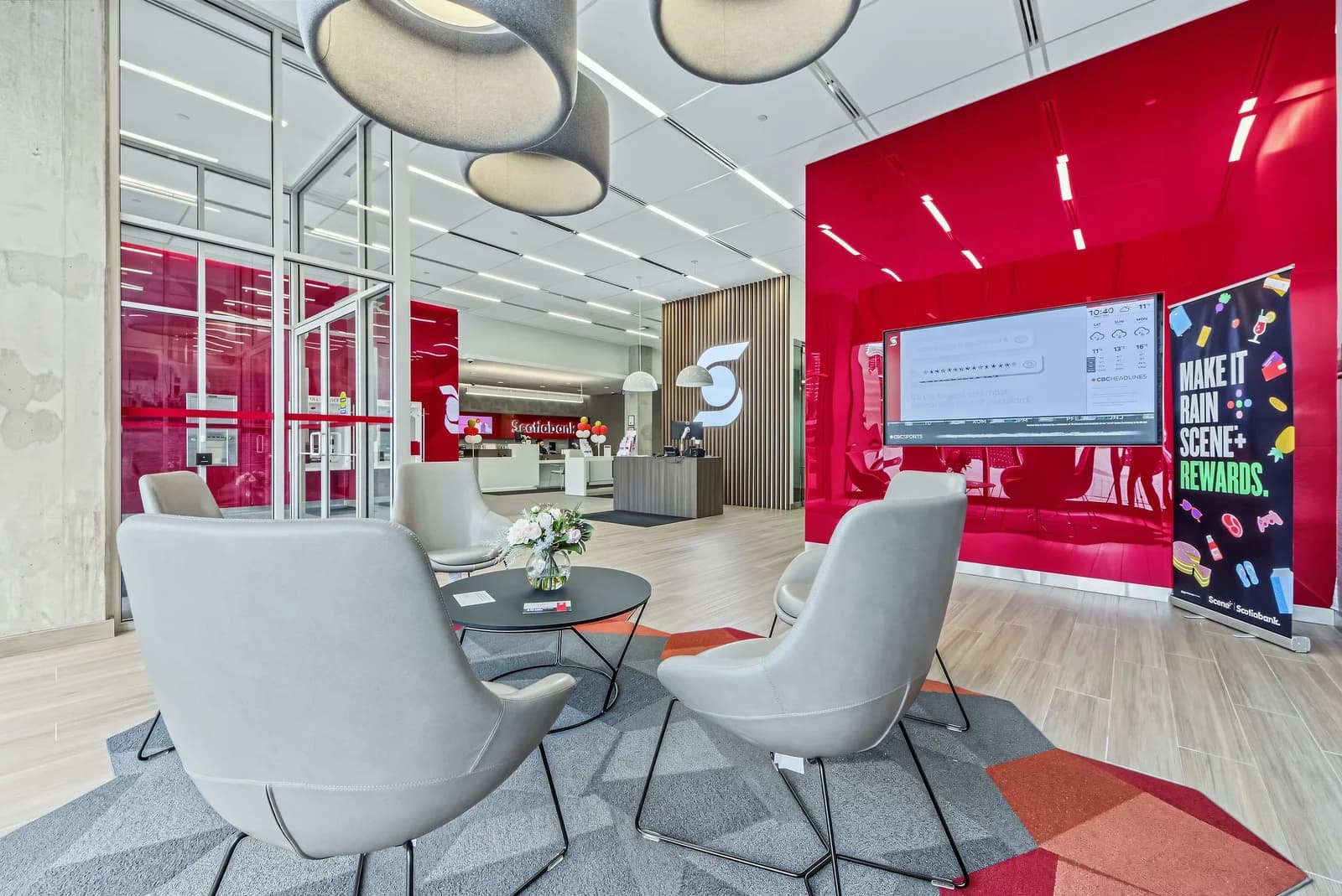 Modern branch interior with a lounge of grey armchairs, a red glass feature wall, a digital display and pendant lighting