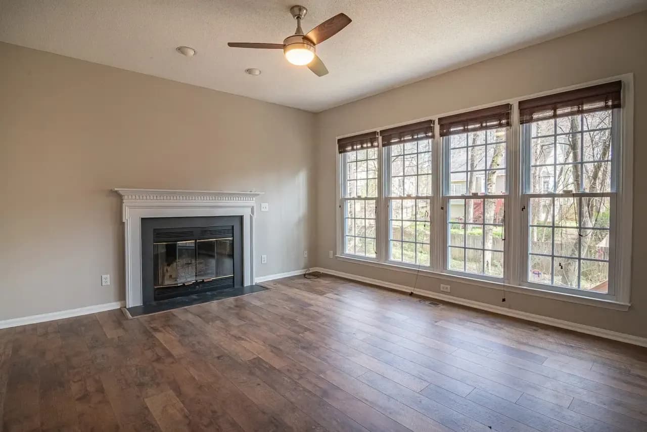 Empty room with a fireplace, ceiling fan and corner windows before virtual staging