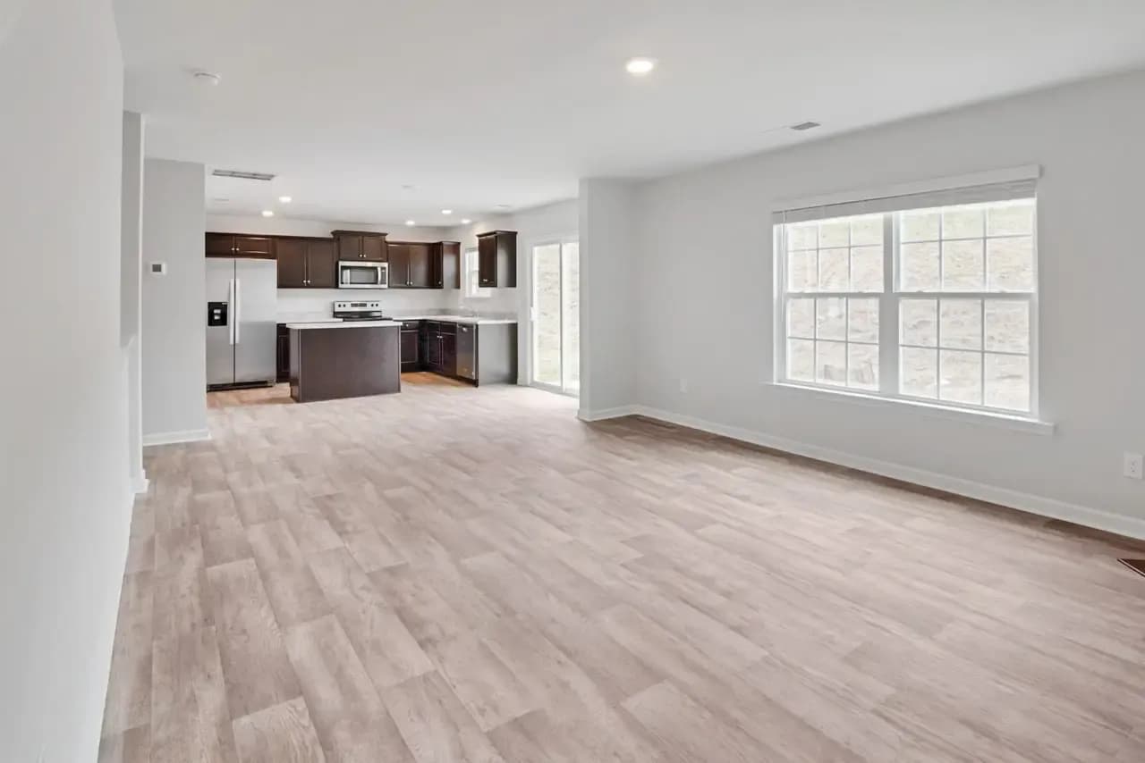 Empty open-plan room with a large window adjoining a kitchen before virtual staging